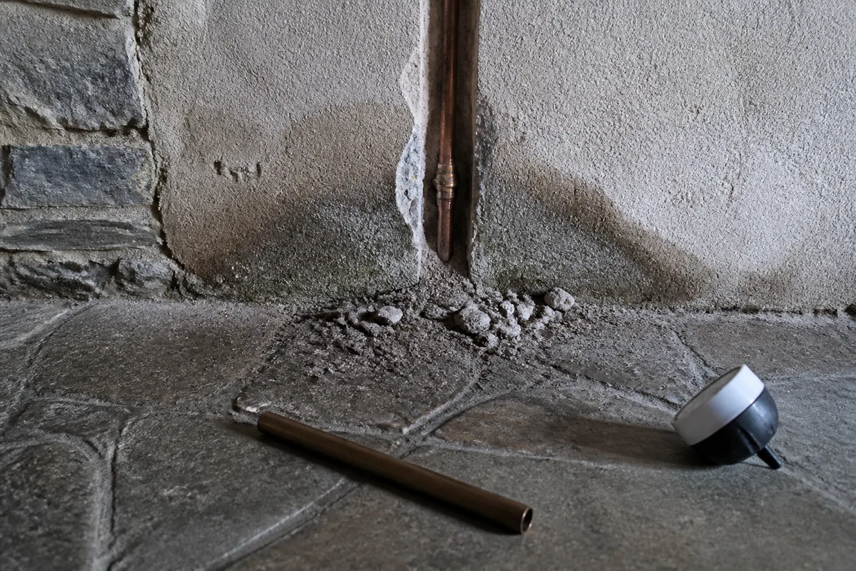 Bas de mur en granit épais ouvert sur une saignée étroite laissant apparaître une canalisation de cuivre