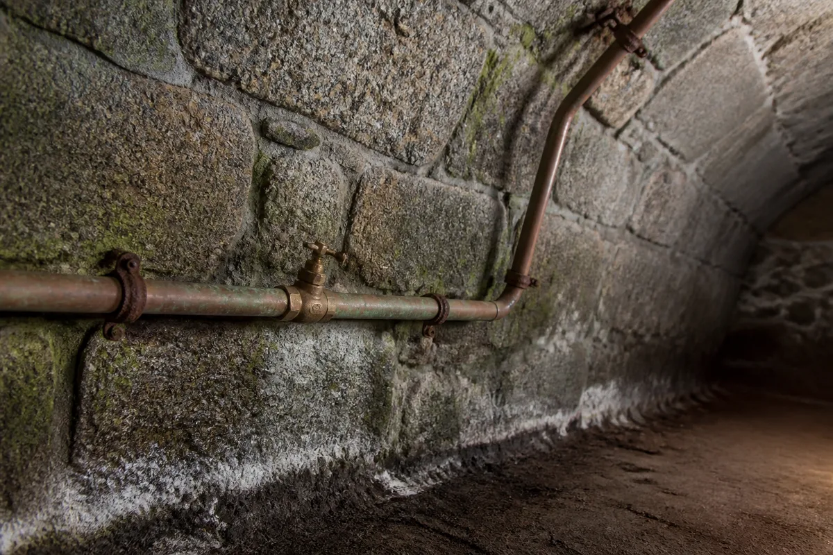 Cave voûtée de granit avec tube de cuivre patiné et trace d&rsquo;humidité au bas du mur