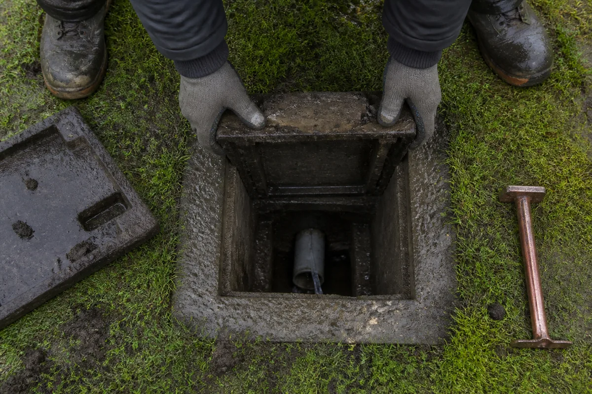 Regard de visite ouvert dans une pelouse humide laissant voir une canalisation en PVC