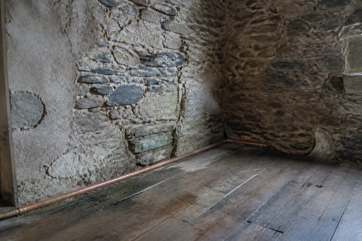Mur de granit et de schiste ouvert au pied d’un plancher bois, canalisation de cuivre apparente